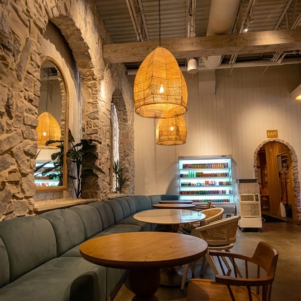 Cozy restaurant interior with stone walls, woven pendant lights, blue booth seating, and wooden tables.