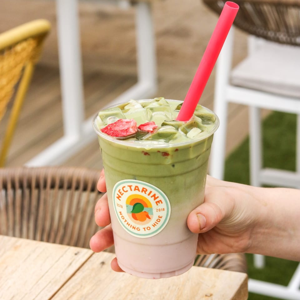 Iced matcha with a pink straw in a Nectarine logo cup held above a table.