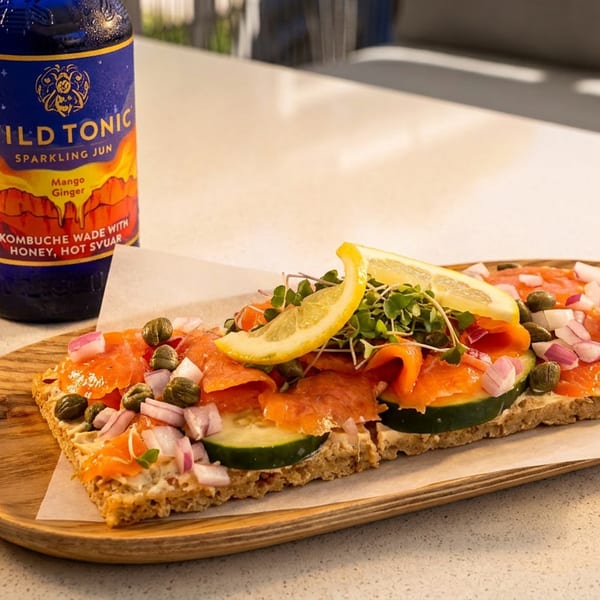 Smoked salmon toast with capers, red onion, cucumber, and lemon, next to a Wild Tonic kombucha.