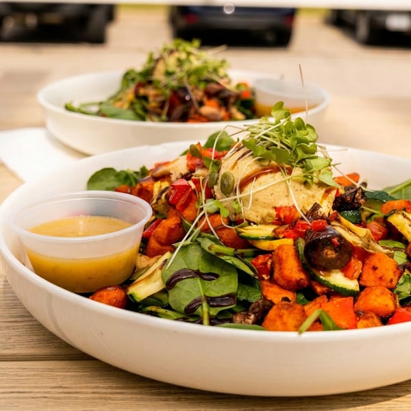 Two vibrant salads with roasted vegetables, hummus, and microgreens on a wooden outdoor table.