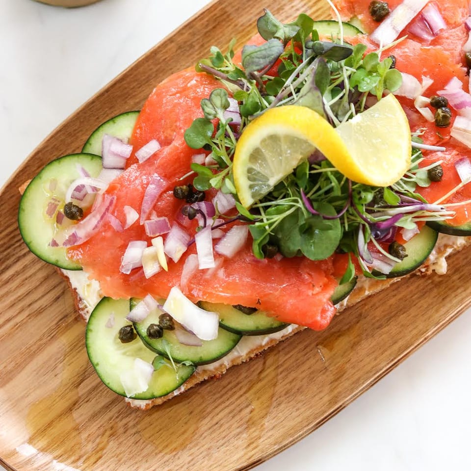 Salmon toast with cucumber, capers, red onion, greens, and lemon.