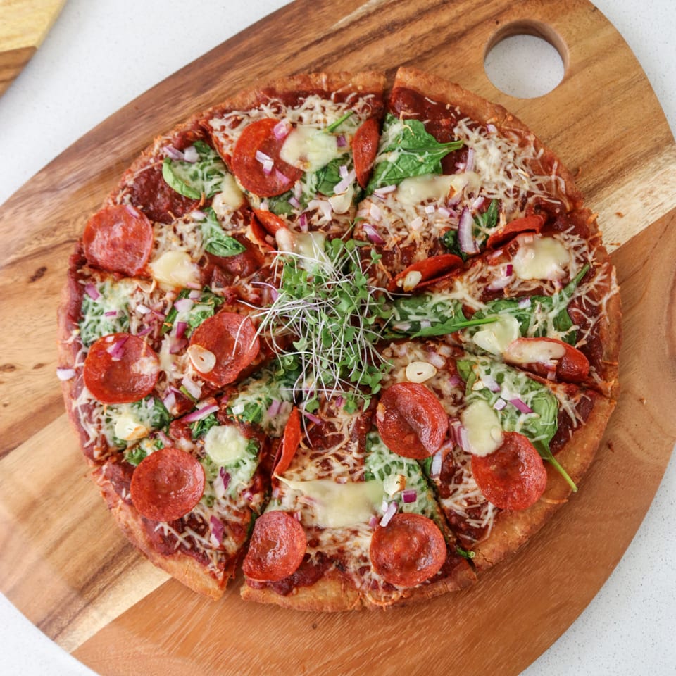 Pepperoni pizza with greens on a wooden board.